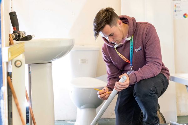 A plumbing student marks a line on a piece of pipe.