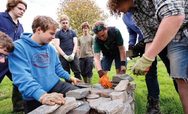 Group of students and tutor building a brick country wall