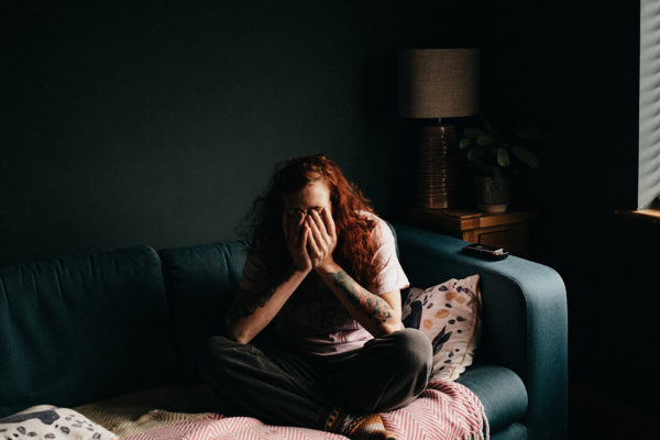 A distressed person in a dark room sitting alone on a sofa
